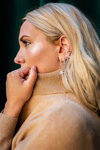 Side view of female with long blond hair and in stylish outfit standing near green building in city and looking away