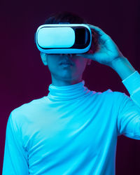 Young man using virtual reality simulator against colored background