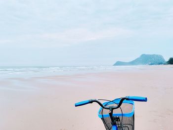 Blue bicycle at beach against sky