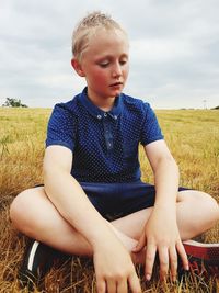 Cute thoughtful boy sitting on grassy field