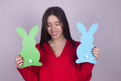 Smiling woman holding paper eater bunny against gray background