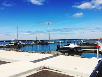 Sailboats moored at harbor against blue sky