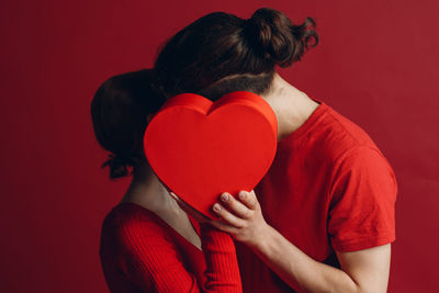 Midsection of woman holding red heart shape against wall