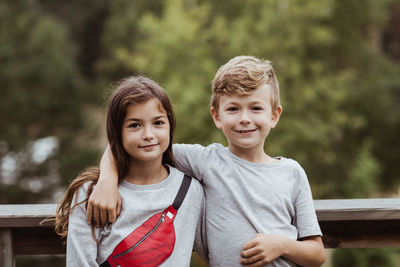 Portrait of smiling brother arm around standing with sister against railing