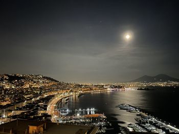 Illuminated city by sea against sky at night