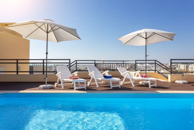 Lounge chairs by swimming pool against clear sky