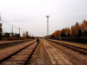 Rear view of man walking on railroad track against sky