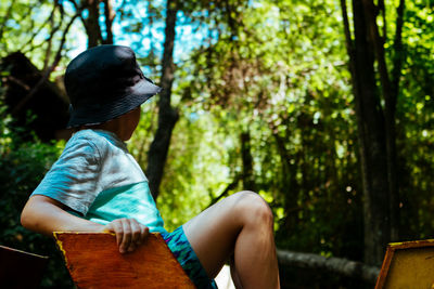 Side view of boy sitting on rock in forest