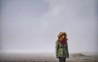 Woman looking away while standing on field during foggy weather