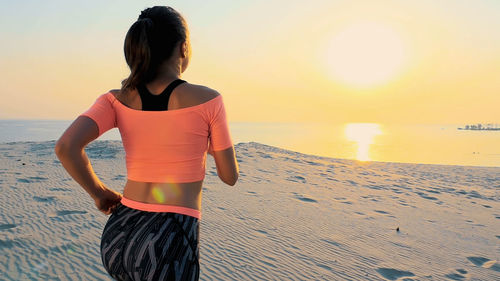 Side view of woman standing at beach against sky during sunset