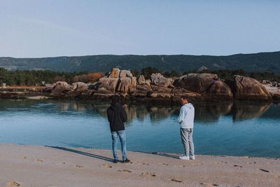 Rear view of people walking on beach against clear sky