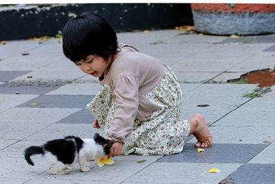 Cute girl playing with kitten on footpath