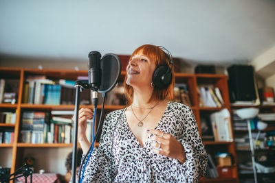 Female vocalist in headset singing song into mic with pop filter during record process at home