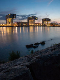 Illuminated buildings by river against sky at dusk