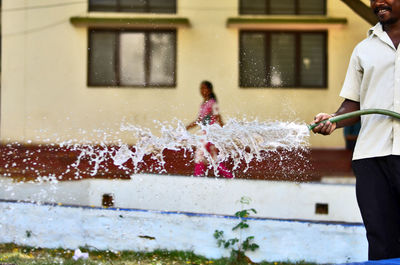 Midsection of man splashing water with garden hose