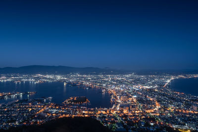 High angle view of illuminated cityscape against clear blue sky