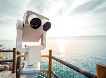 Close-up of coin-operated binoculars by sea against sky