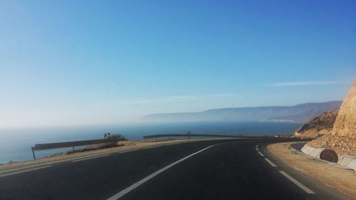 Road by sea against clear blue sky