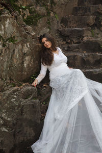 Bride wearing white wedding dress sitting on rocks