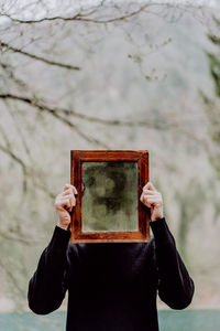 Portrait of woman holding camera while standing against tree