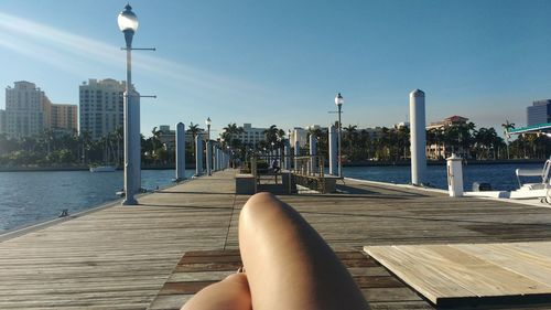 Low section of woman relaxing on pier over river in city