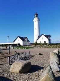 Lighthouse by building against clear blue sky