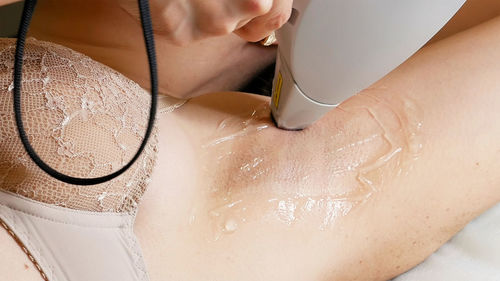 Cropped hand of woman applying gel on female customer armpit in spa