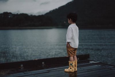 Rear view of boy looking at lake while standing during sunset