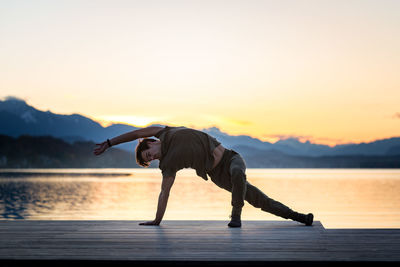 Man with arms outstretched on lake against sky during sunset