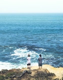 Rear view of men standing at beach against clear sky