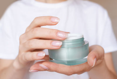 Female hands with natural pink manicure holding a transparent cream jar. beauty product presentation 