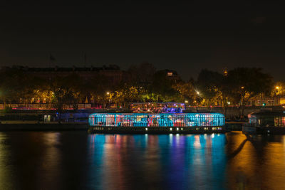 Illuminated buildings by river against sky at night