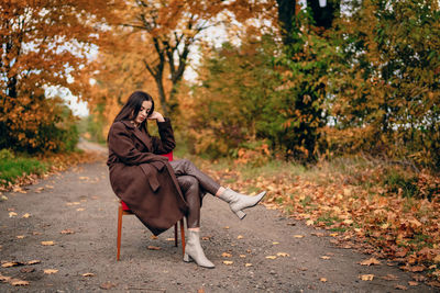 Young beautiful woman with old armchair on the country lane in autumn