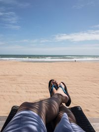 Low section of man lying on sand at beach against sky