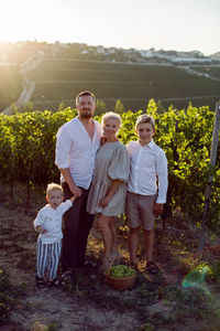 Family with children, boys, stands in a grape field at sunset with a basket of green berries