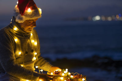 Statue by illuminated sea against sky at night