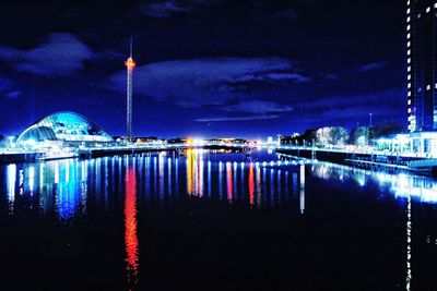 Illuminated city by river against sky at night