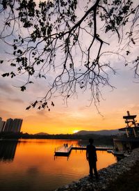 Silhouette person standing by lake against sky during sunset