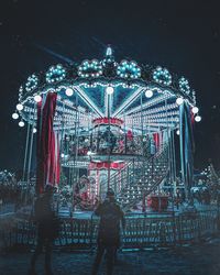 Rear view of people at amusement park against sky at night