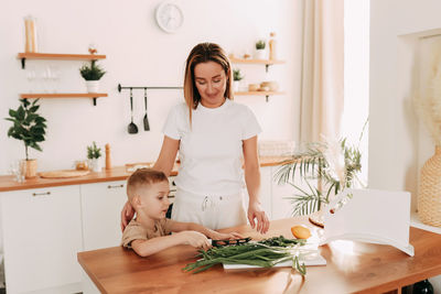 A young mother and a small child prepare lunch together in the cozy bright kitchen of indoors