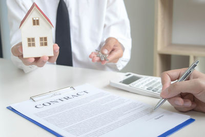 Midsection of real estate agent giving keys while client signing contract 