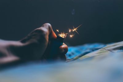 Cropped hand igniting cigarette lighter on bed