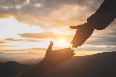 Cropped image of hand against sky during sunset