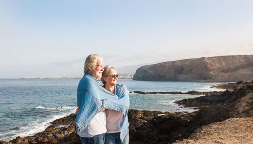 Smiling couple looking away while standing at beach