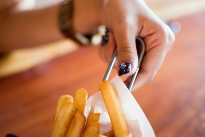 Cropped hand of woman having french fries on table