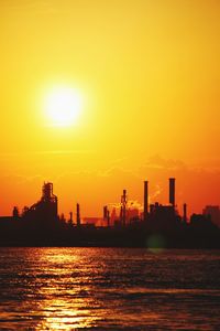 Silhouette buildings by sea against sky during sunset