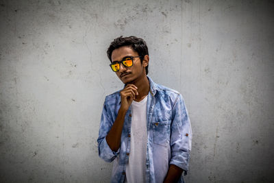 Man wearing sunglasses standing against wall