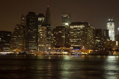 Illuminated buildings by river against sky at night