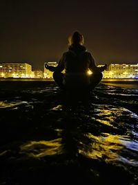 Rear view of man sitting on illuminated cityscape at night
