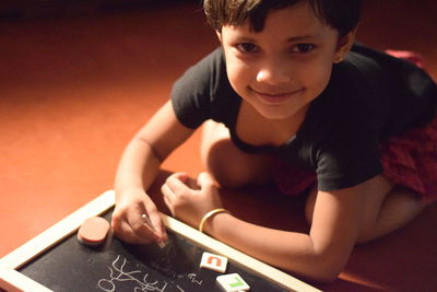 Portrait of girl writing on slate while kneeling on floor at home